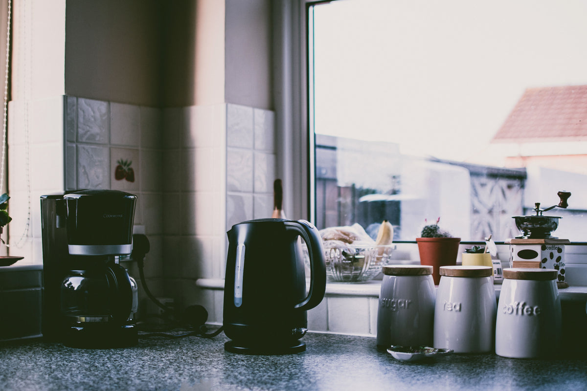Cozy kitchen scene with coffee maker, kettle, and jars on a sunny counter.