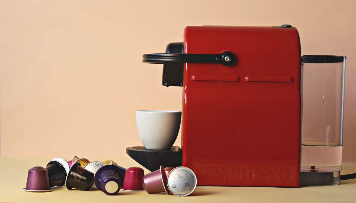 Red coffee machine with assorted capsules and a cup on a beige background.
